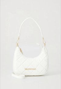 Quiltet hvit Valentino-veske med gull-logo, kort håndtak og avtakbar skulderrem på ensfarget bakgrunn.