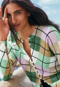 Cardigan en maille à motif de plaid vert, rose, blanc et beige ; doté d'un col rond et de boutons blancs sur le devant.
