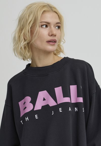 Sweat-shirt noir avec le mot "BALL" en grosses lettres roses et un texte plus petit "THE JEANS" en dessous. Coupe décontractée, col côtelé et texture douce.