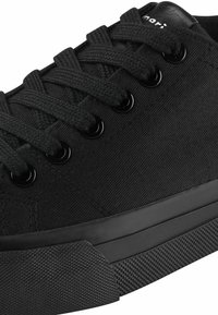 Black canvas sneaker with flat laces, metal eyelets, rubber sole, and textured toe cap. Features minimalistic design and smooth finish.