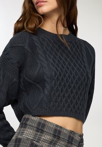 Maglione corto a coste grigio scuro con motivi testurizzati, scollatura rotonda e orlo a costine, abbinato a una gonna a quadri a vita alta.