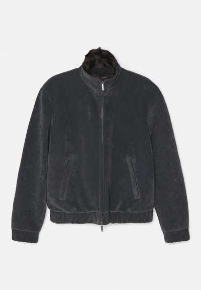Veste bomber gris foncé avec une texture lisse, fermeture éclair, col montant et poches latérales ; présente un accent en fausse fourrure douce au niveau du col.