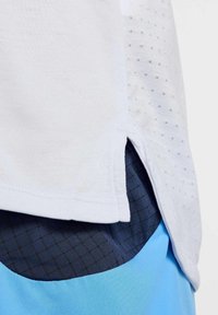Camiseta atlética blanca con un tejido texturizado y pequeños orificios, sobrepues ta a pantalones cortos azul oscuro con un patrón de cuadrícula y acentos azul claro.