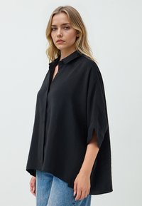 Black half-sleeve shirt with a collared neckline, made of lightweight fabric. Features a relaxed fit and side slits for comfort.