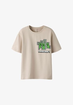 T-shirt beige à manches courtes avec un design Minecraft présentant trois personnages Creeper verts pixellisés au-dessus du logo Minecraft sur la poitrine.