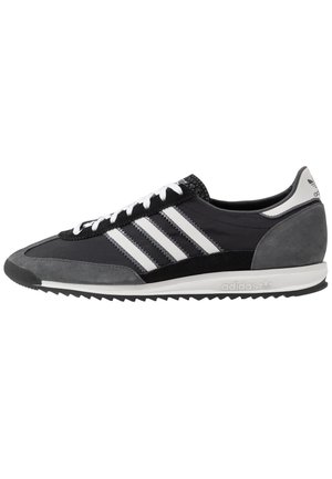 Czarno-szary sneaker Adidas z białymi paskami, białymi sznurówkami i wytłoczonym logo na śródpodeszwie, pokazany z boku na białym tle.