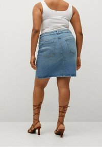 Jupe en denim bleu clair avec une coupe ajustée, dotée de deux poches arrière, ourlet au-dessus du genou, associée à des talons marron à lanières.