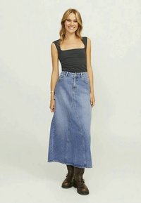 Sá de ganga maxi em azul claro, com cintura alta, formato em A e detalhes de costura na frente, combinada com uma camisola justa preta e botas castanhas.