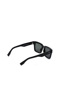 Lunettes de soleil rectangulaires noires avec montures épaisses et verres foncés vues de dos sur fond blanc.