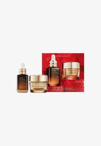 Set mit drei Estee Lauder Hautpflegeprodukten: eine dunkelbraune Tropfflasche, ein Gold akzentuiertes Glas und eine rote Geschenkbox mit kreisförmigen Mustern.