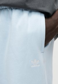 Ανοιχτό μπλε αθλητικό σορτς από μαλακό ύφασμα, με λευκό λογότυπο Adidas στο μπούτι και ελαστική ζώνη μέσης για άνεση.