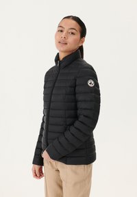 Giubbotto imbottito nero con colletto alto, design trapuntato, zip completa e un patch logo sulla manica sinistra. Tessuto liscio e leggero.