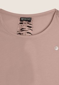T-shirt rose clair avec un col rond, texture douce, avec une étiquette à motifs noirs et beiges et un petit logo argenté en bas à droite.