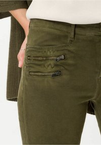 Pantalones verde oliva hechos de una tela suave, con tres bolsillos con cremallera y una textura lisa. Corte relajado con una cinturilla estándar.
