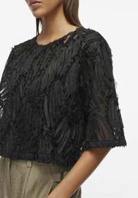 Top negro de mangas cortas con tejido de rizo texturizado, adornado con diseños en capas. Escote redondeado, paneles transparentes y fit corto.