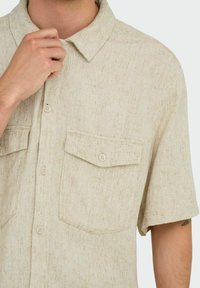 Lys beige kortærmet skjorte med knapper, lavet af struktureret stof, med to forlommer og en standard krave med matchende knapper.