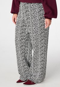 Zwart-witte zebraprint wijde broek met een zachte textuur. Draagt bijpassende puntige bordeauxrode hakken met een strak en taps toelopend ontwerp.