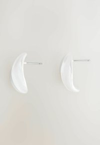 Cercei din ceramică albă cu o formă de semilună, având un finisaj lucios și poste metalice de culoare argintie pentru atașare.