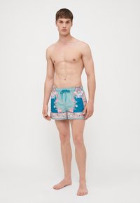 Ανδρικό μαγιό σε ανοιχτό θαλασσί με λουλουδάτα και γεωμετρικά σχέδια, κορδόνι στη μέση και αντίθετες μπλε πλαϊνές πάνελ. Μαλακή υφή υφάσματος.