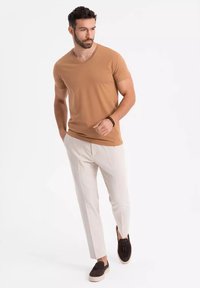 Hnědý v-neck t-shirt v kombinaci s krémovými zúženými kalhotami a tmavě hnědými nazouvacími botami. Hladká látka a přiléhavý střih zdůrazňují moderní vzhled.