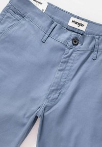 Jasnoniebieskie bawełniane spodnie z zapięciem na guzik, paskami na pasek i bocznymi kieszeniami. Posiadają subtelne detale stębnowania oraz metkę Wrangler na talii.