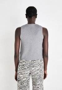 Un top gri, fără mâneci, cu o textură netedă, asociat cu pantaloni cu talie înaltă, având un model cu dungi de zebra alb-negru.