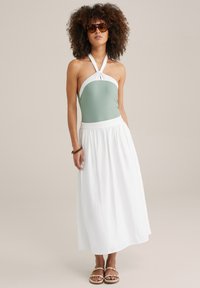 Costume da bagno verde e bianco con scollatura a halter abbinato a una maxi gonna bianca fluida e sandali marroni, caratterizzati da una texture liscia e una vestibilità rilassata.