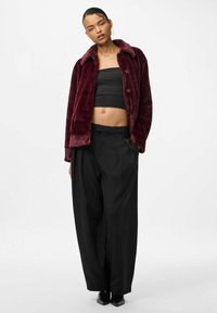 Bordeaux falsk pelsjakke med spids krave, sort cropped top, højtaljede sorte bukser og sorte sko, der har en afslappet silhuet.