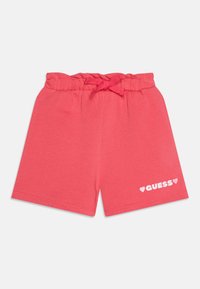 Korallenfarbene Shorts aus weichem Baumwollmaterial, mit einem elastischen Bund und Bändchen sowie dem weißen "GUESS"-Logo mit Herzen auf der unteren linken Vorderseite.