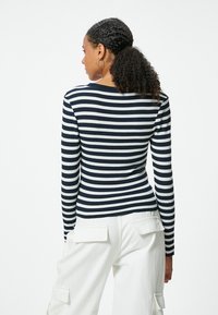 Gestreiftes Langarmoberteil in Marineblau und Weiß mit horizontalen Streifen, rundem Ausschnitt und tailliertem Design. Getragen mit weißen Cargo-Hosen.