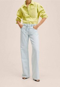 Camicia di jeans verde chiaro con taschino sul petto, abbinata a jeans azzurri a vita alta con coulisse, fit rilassato e una trama sottile.