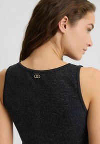 Schwarzes Tanktop aus strukturiertem Stoff mit schimmernden Akzenten, veredelt mit einem goldfarbenen Hardware-Detail am Rückenausschnitt.