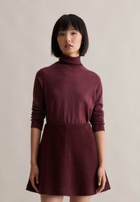 Burgundowy golf z długimi, dopasowanymi rękawami w połączeniu z dopasowaną spódnicą, która ma teksturowane wykończenie i rozkloszowany dół.