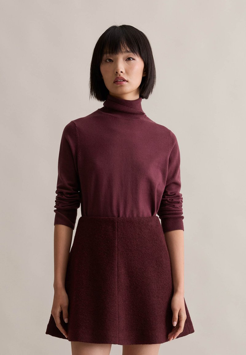 Burgundowy golf z długimi, dopasowanymi rękawami w połączeniu z dopasowaną spódnicą, która ma teksturowane wykończenie i rozkloszowany dół.