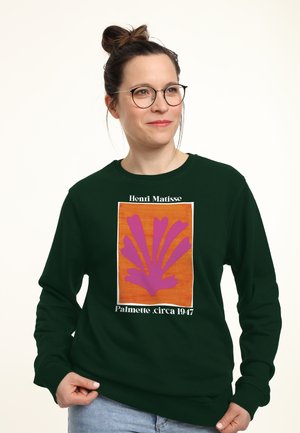 Kvinde med briller og hår i en knold iført en mørkegrøn sweatshirt med et pink og orange Henri Matisse Palmette-print, cirka 1947.