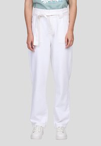 Pantalon en coton blanc avec une ceinture, présentant une coupe droite et deux poches avant, associé à des baskets blanches.