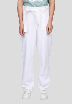 Pantalon en coton blanc avec une ceinture, présentant une coupe droite et deux poches avant, associé à des baskets blanches.