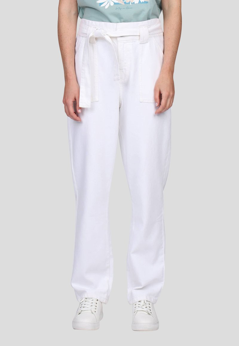 Pantalon en coton blanc avec une ceinture, présentant une coupe droite et deux poches avant, associé à des baskets blanches.