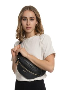 Marsupio in pelle nera con forma arrotondata, chiusura in oro e scomparto con zip, tenuto da una persona che indossa una semplice maglietta bianca.