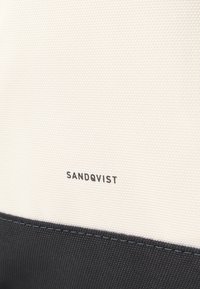 Platnena torba s teksturiranim bijelim gornjim dijelom i crnim donjim dijelom, s logotipom "SANDQVIST" tiskanom u crnoj boji.