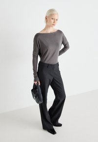 Gray long-sleeve top with an off-shoulder design, paired with tailored black trousers and a textured dark bag featuring a polka dot pattern.