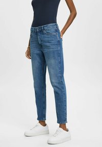 Jeans i medelblått, slim-fit design med avsmalnande ben, fem fickor och knappgylf, ihop med vita sneakers.