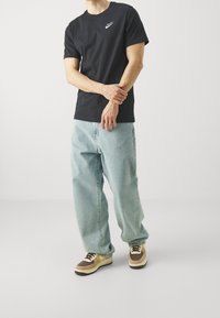 Black cotton T-shirt with white Nike logo, paired with light blue loose-fitting jeans and brown and cream sneakers. Simple design, casual fit.