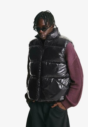 Puffer vest in glossy black fabric, featuring a high collar, front zipper, and contrasting textured purple sleeves. Minimal branding visible.
