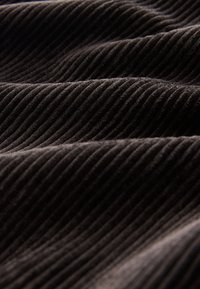 Brązowa prążkowana tkanina o miękkiej fakturze, z równoległymi liniami i zagięciami, ukazująca głębię i wymiar materiału.