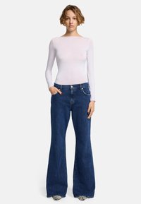 Top bianco a maniche lunghe con scollo a girocollo abbinato a jeans svasati blu con design a cinque tasche e dettagli argentati.