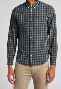 Camicia a maniche lunghe a quadri in blu scuro e nero con dettagli bianchi, colletto button-down e taschino sul petto. Tessuto morbido con design aderente.