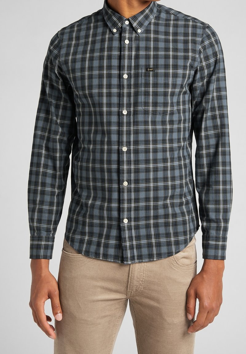 Camicia a maniche lunghe a quadri in blu scuro e nero con dettagli bianchi, colletto button-down e taschino sul petto. Tessuto morbido con design aderente.