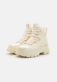 Kremfargede høye sneakers med glanset overflate, tykk plattformsåle, teksturert detaljer og flate lisser. Har polstret krage.