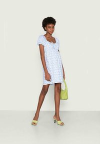 Vestido azul com estampado floral, mangas curtas bufantes, decote redondo e corpete ajustado. Combinado com uma bolsa verde e sandálias de salto aberto a condizer.